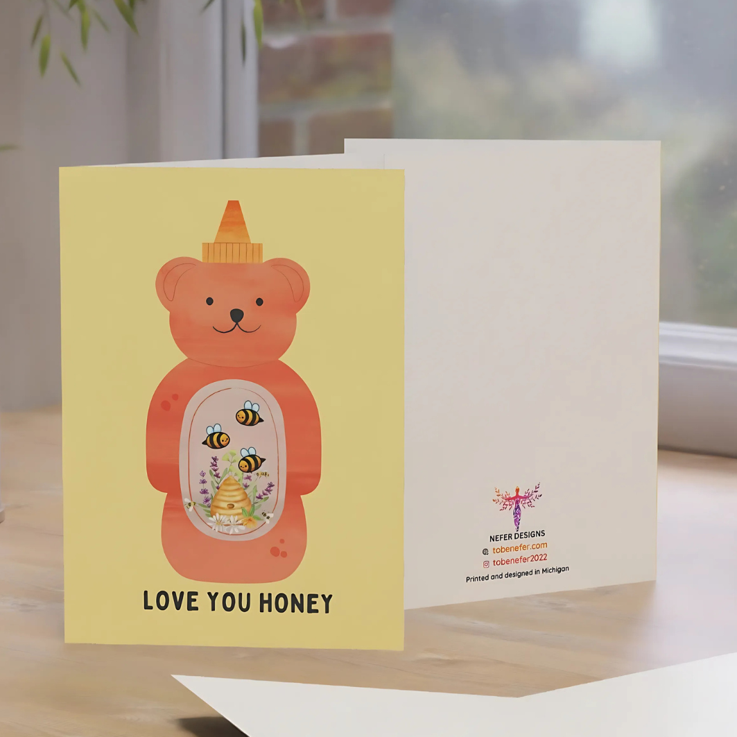 Greeting card with a bear-shaped honey bottle design on a wooden surface.