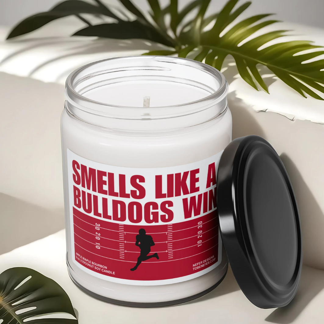 A Georgia Bulldogs-themed soy candle with a label that says 'Smells Like a Bulldogs Win | Lucky Game Day,' sitting on a marble surface