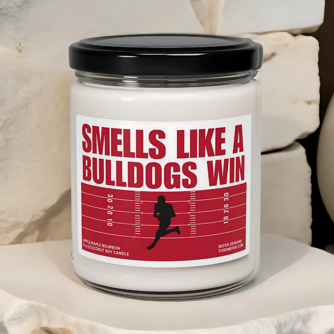A Georgia Bulldogs-themed soy candle with a label that says 'Smells Like a Bulldogs Win | Lucky Game Day,' sitting on a marble surface