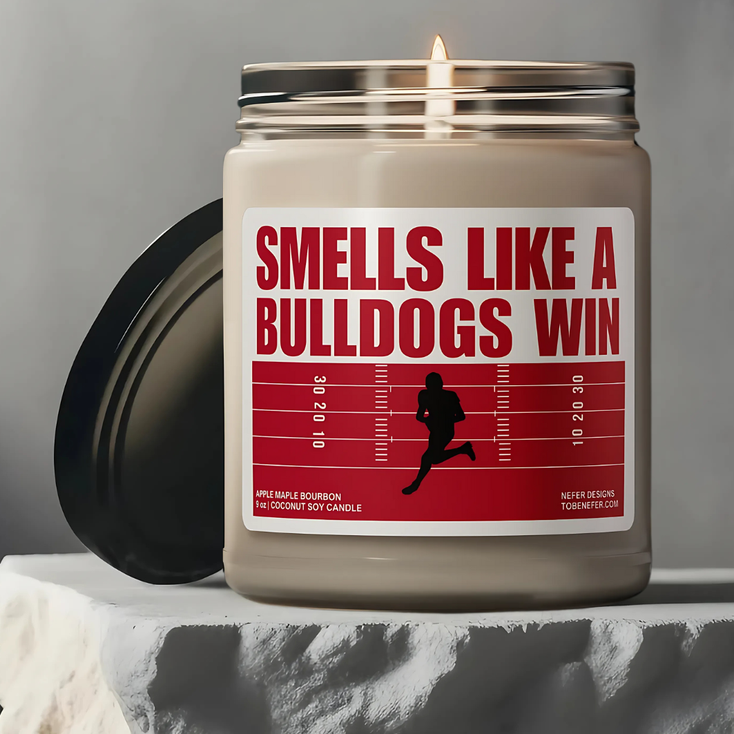 A Georgia Bulldogs-themed soy candle with a label that says 'Smells Like a Bulldogs Win | Lucky Game Day,' sitting on a marble surface