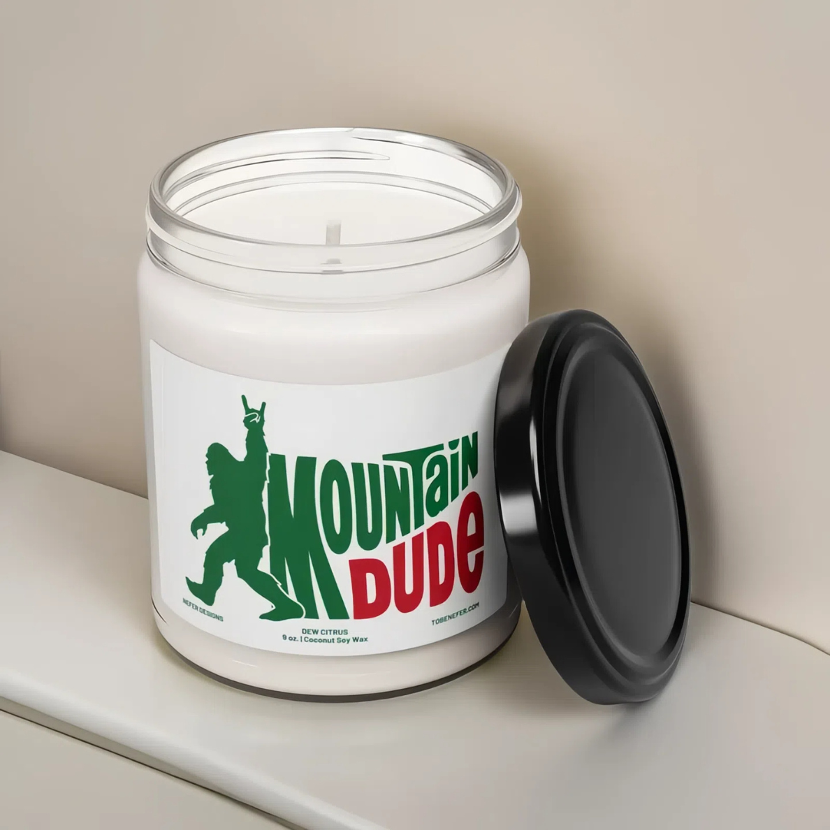 A 9 oz Mountain Dude Soda Pop Soy Candle in a jar, featuring a vibrant bigfoot design with the wording of mountain dude. The candle is hand-poured with a coconut and soy wax blend, offering a refreshing lemon-lime soda scent. Perfect for soda lovers and nostalgia enthusiasts.