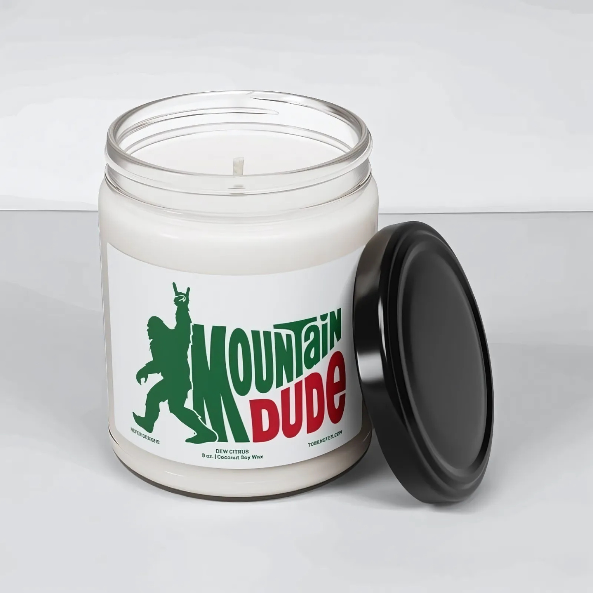 A 9 oz Mountain Dude Soda Pop Soy Candle in a jar, featuring a vibrant bigfoot design with the wording of mountain dude. The candle is hand-poured with a coconut and soy wax blend, offering a refreshing lemon-lime soda scent. Perfect for soda lovers and nostalgia enthusiasts.