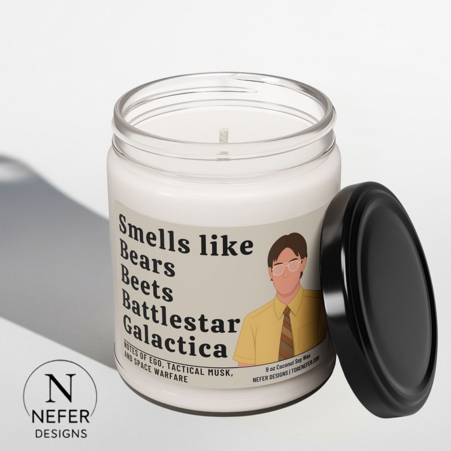 Candle with a label featuring smells like bears, beats and battlestar galactica and a Dwight Schrutz's face, on a light gray background.