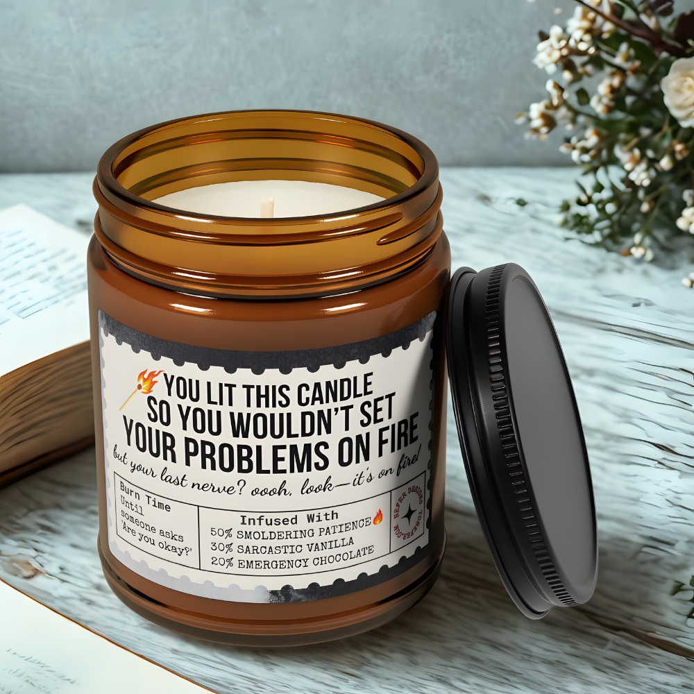 Amber glass 'Last Nerve' candle burning on wooden table, sarcastic label visible ('YOU LIT THIS CANDLE SO YOU WOULDN’T SET YOUR PROBLEMS ON FIRE')