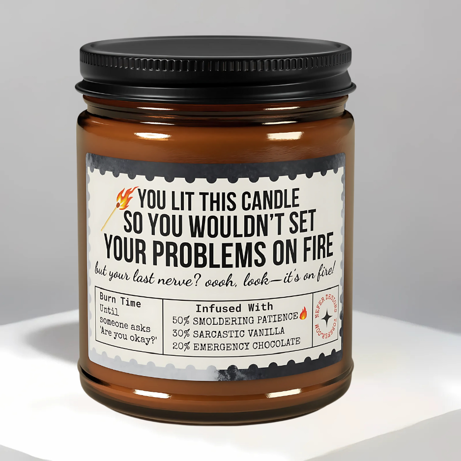Amber glass 'Last Nerve' candle burning on wooden table, sarcastic label visible ('YOU LIT THIS CANDLE SO YOU WOULDN’T SET YOUR PROBLEMS ON FIRE')