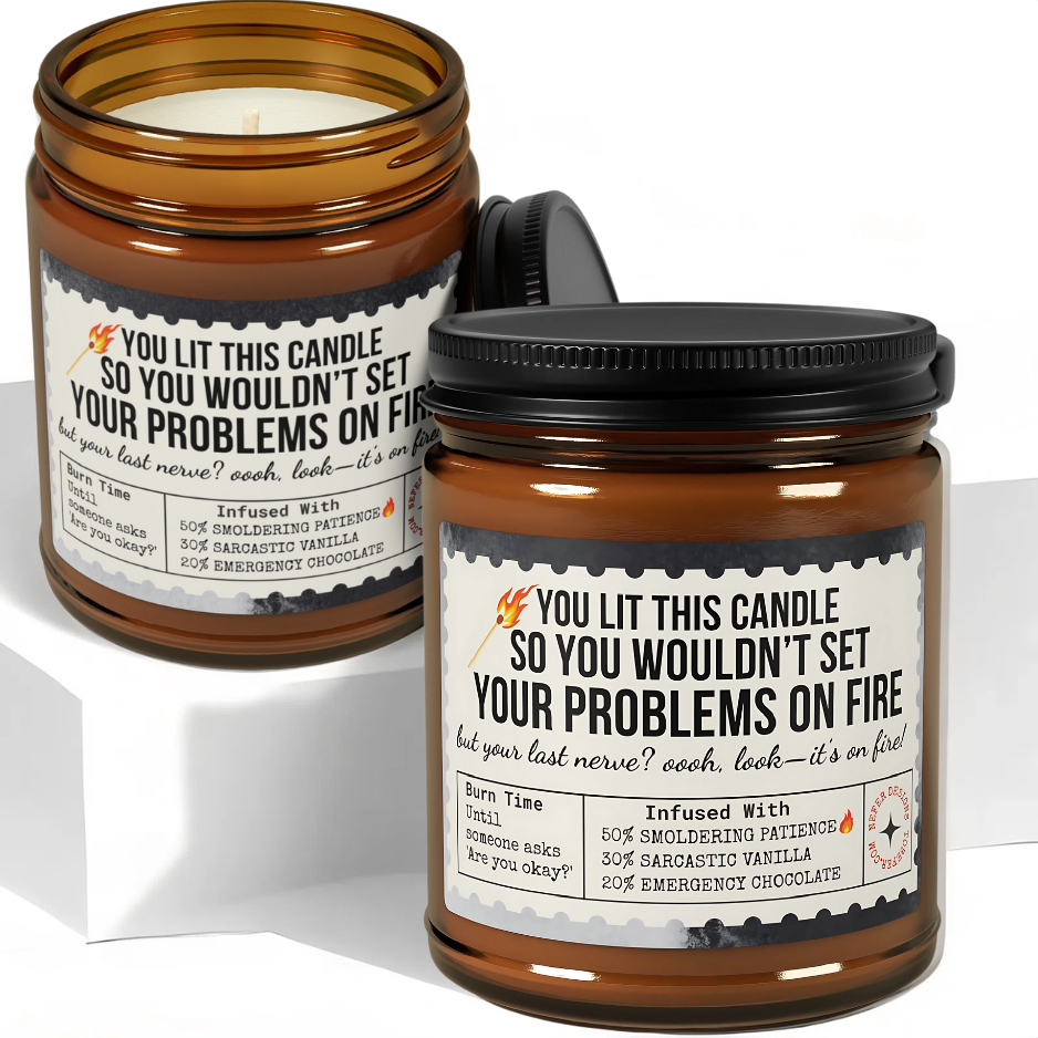 Amber glass 'Last Nerve' candle burning on wooden table, sarcastic label visible ('YOU LIT THIS CANDLE SO YOU WOULDN’T SET YOUR PROBLEMS ON FIRE')