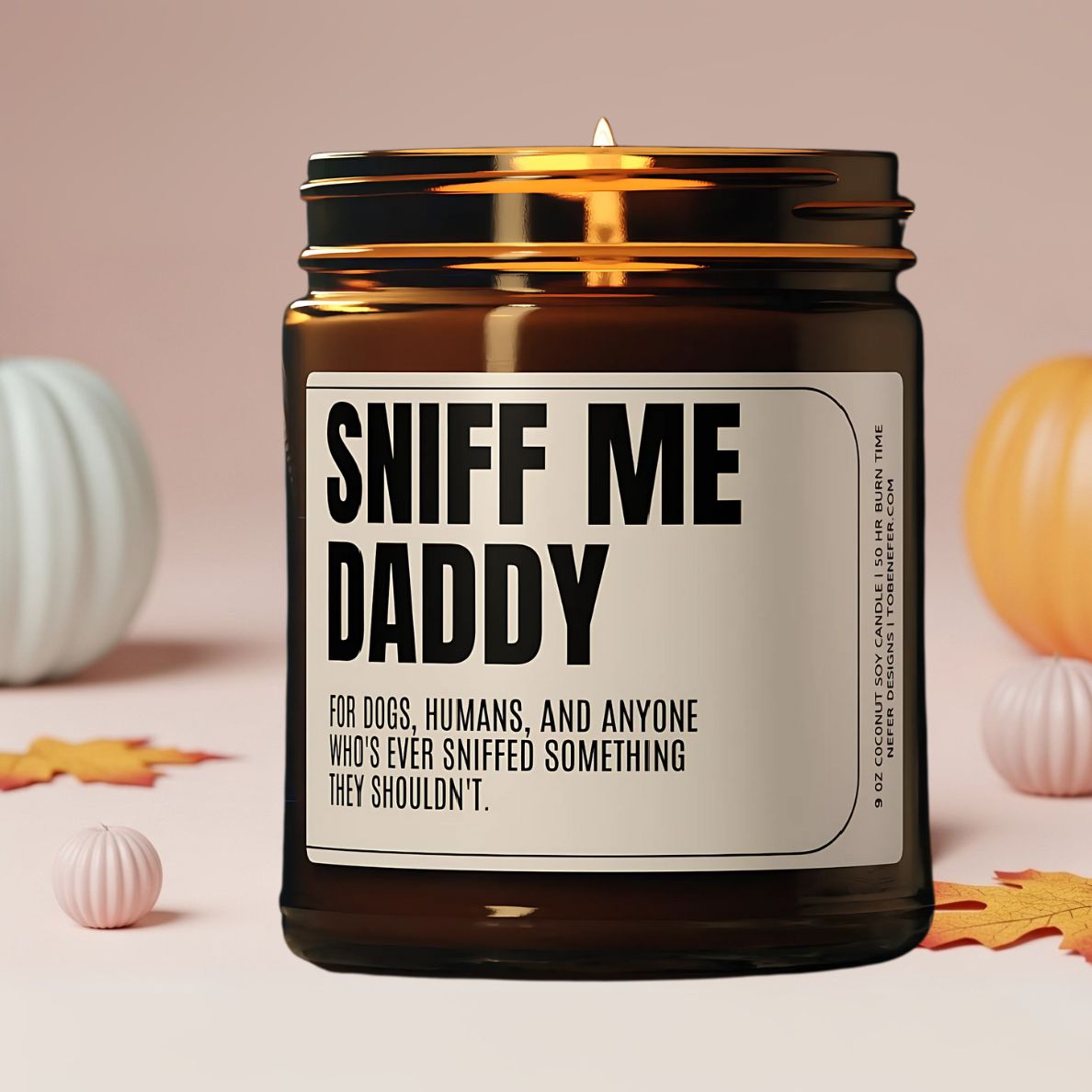Sniff Me Daddy soy candle in a fall-themed setting with scattered autumn leaves and small pumpkins.