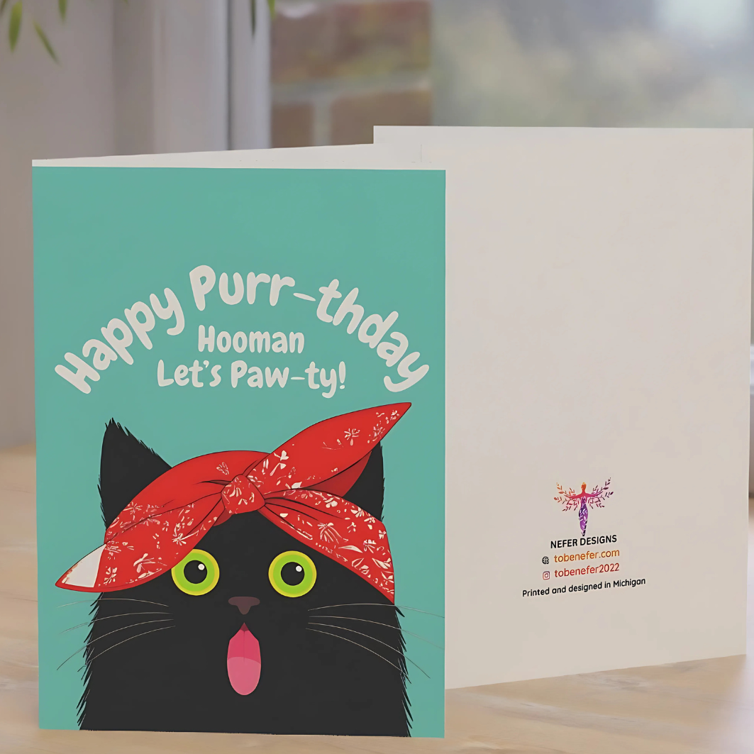 Greeting card with a cat wearing a red bandana and text 'Happy Purr-thday Hooman Let's Paw-ty!' on a teal background placed on a desk. 