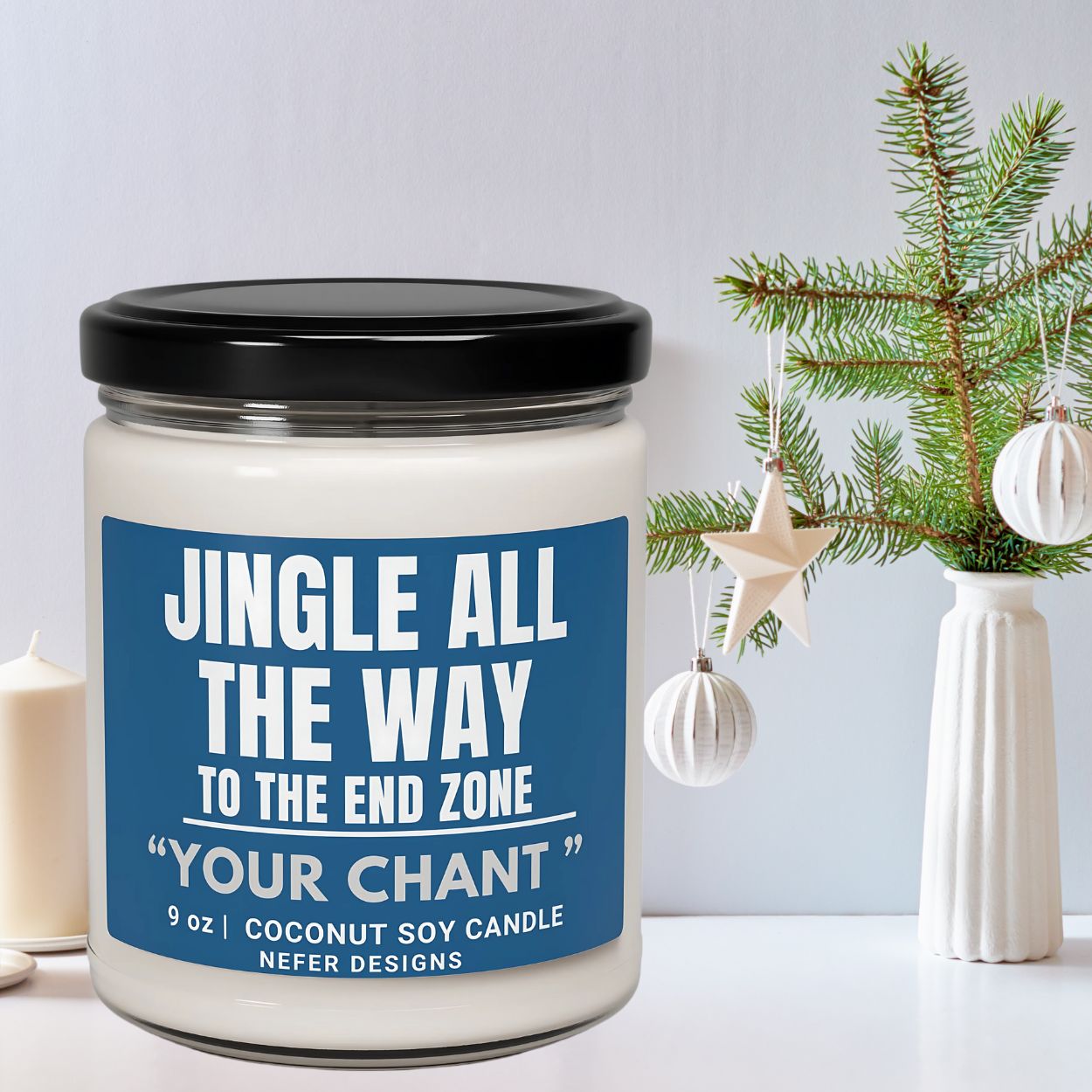Candle jar with blue label and black lid on a white surface with Christmas decorations.