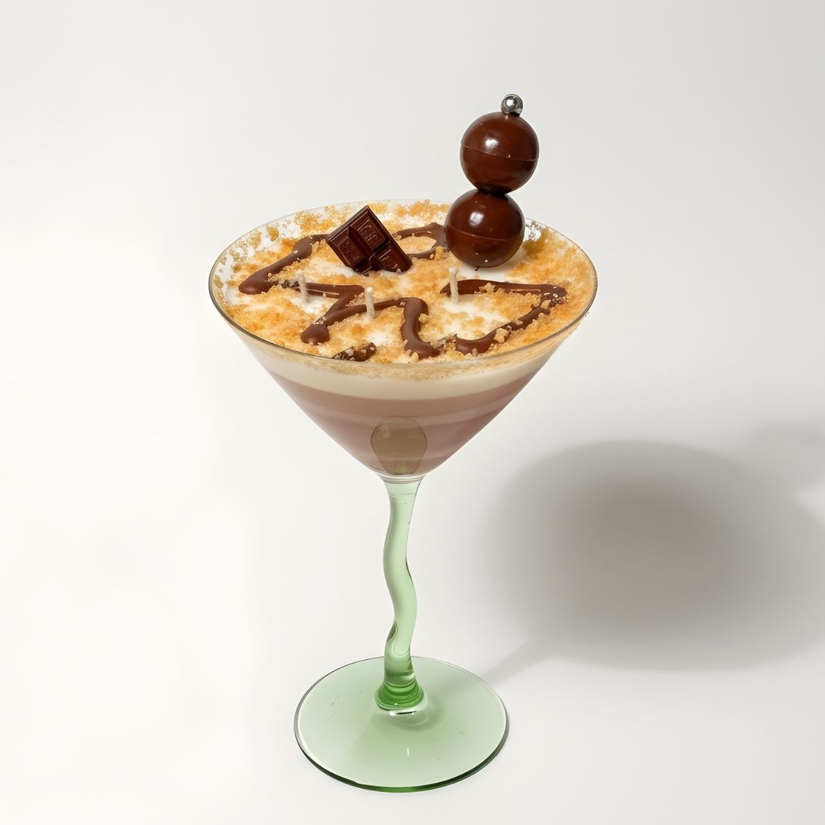 Overhead view of a 10 oz Chocolate Martini dessert candle in a green wavy-stem martini glass. The top of the candle displays intricate chocolate drizzle, a faux sugar rim, and two chocolate sphere embeds, showcasing the unique candle design on a white background.
