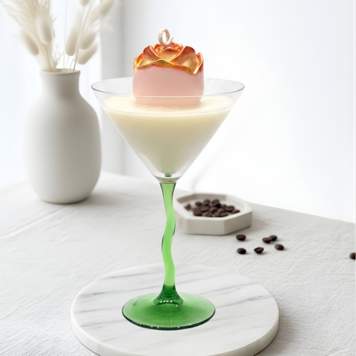 Gilded Rose Martini scented candle in a green wavy-stem glass, staged on a white marble coaster in a bright, modern lifestyle scene with dried florals and coffee beans.