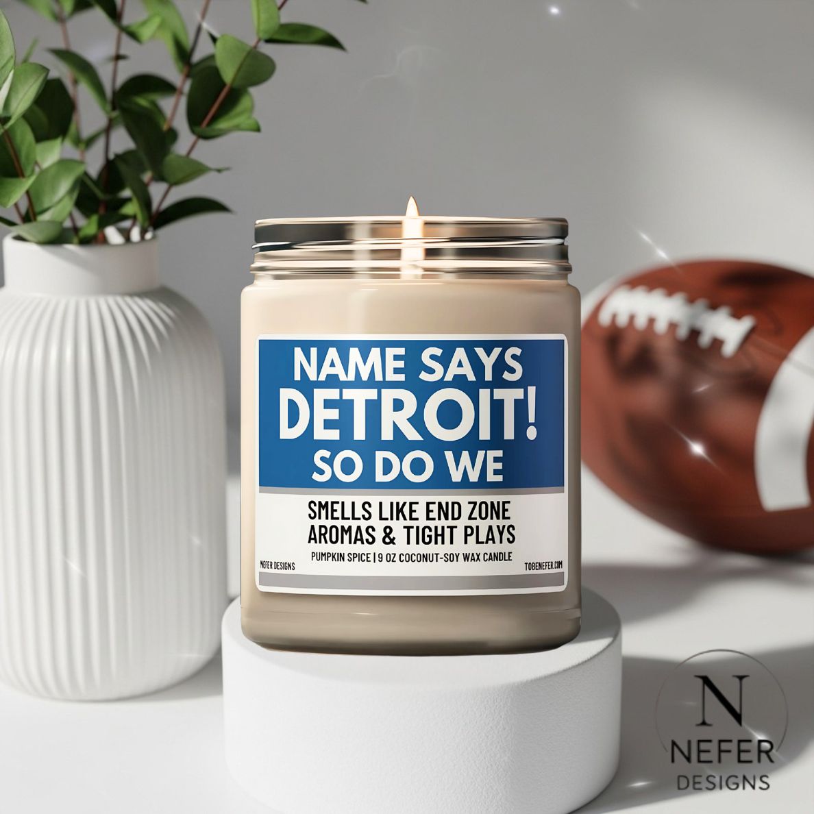 Candle with a label reading 'NAME SAYS DETROIT! SO DO WE' on a white surface with a football and plant in the background.