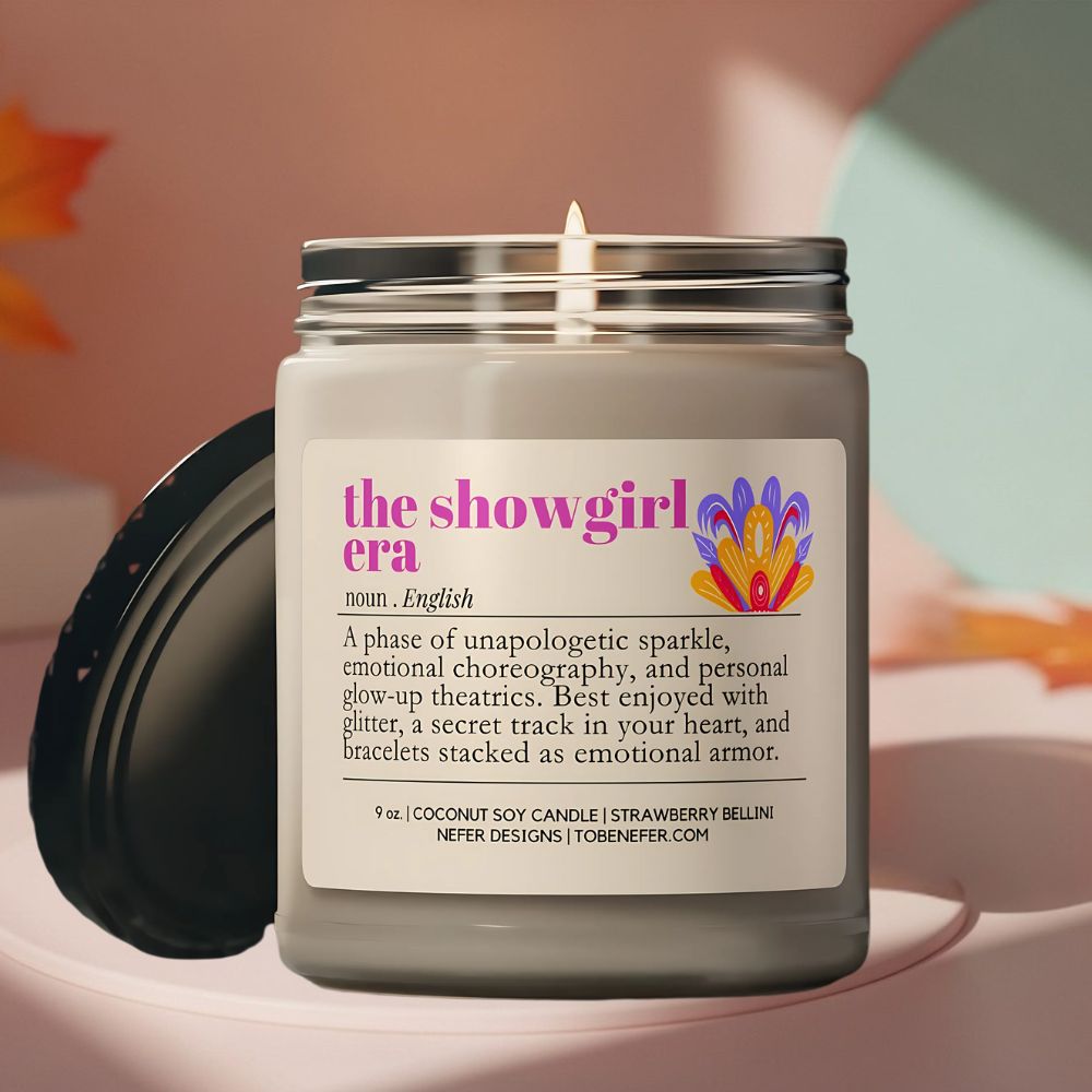 Candle in a jar labeled 'the showgirl era' with a colorful label on a soft background.
