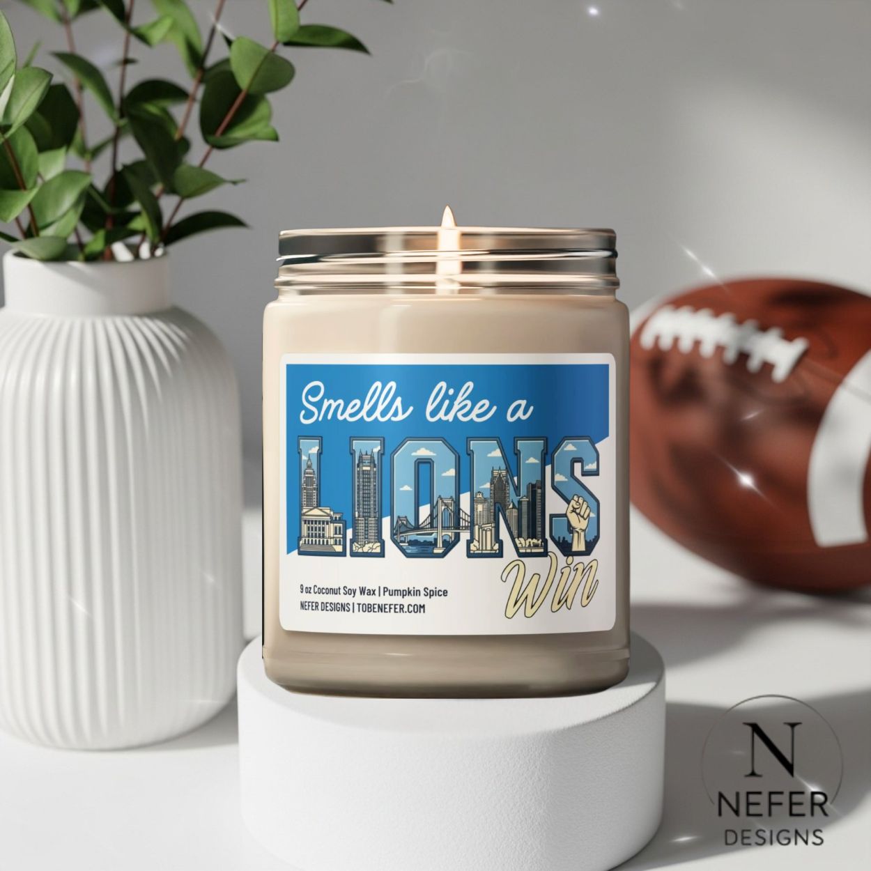 Candle with a 'Smells like a Lions Win' label on a white surface with a football and plant in the background.