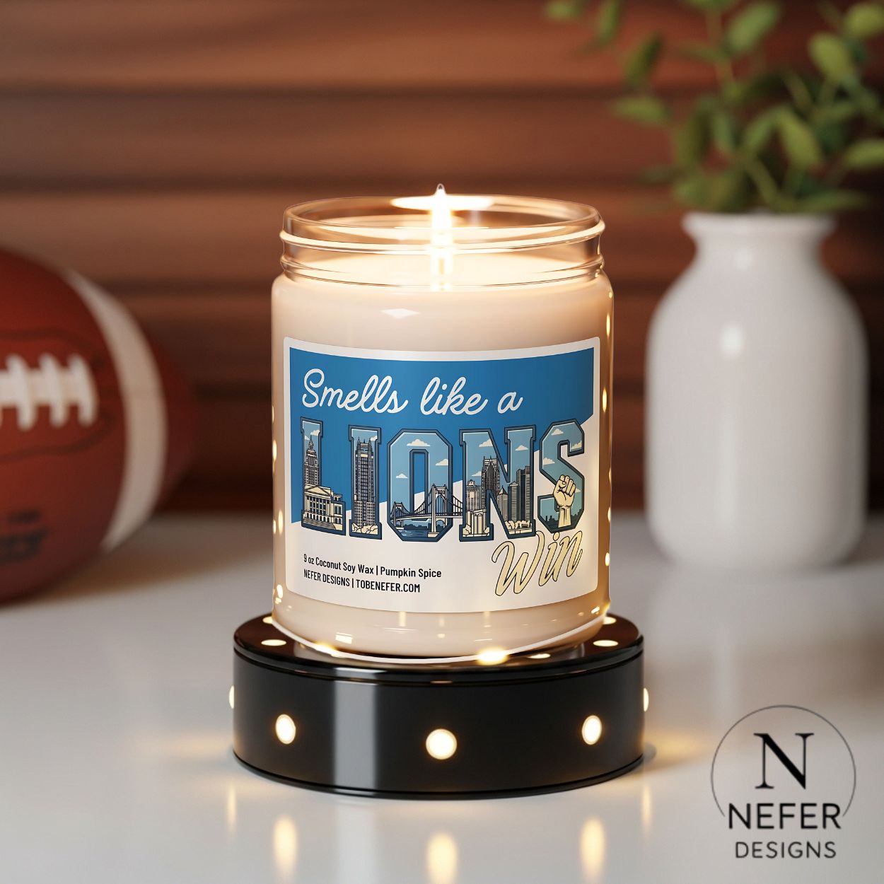 Candle with a label reading 'Smells like a Lions win' on a decorative stand, with sports ball and vase in the background.