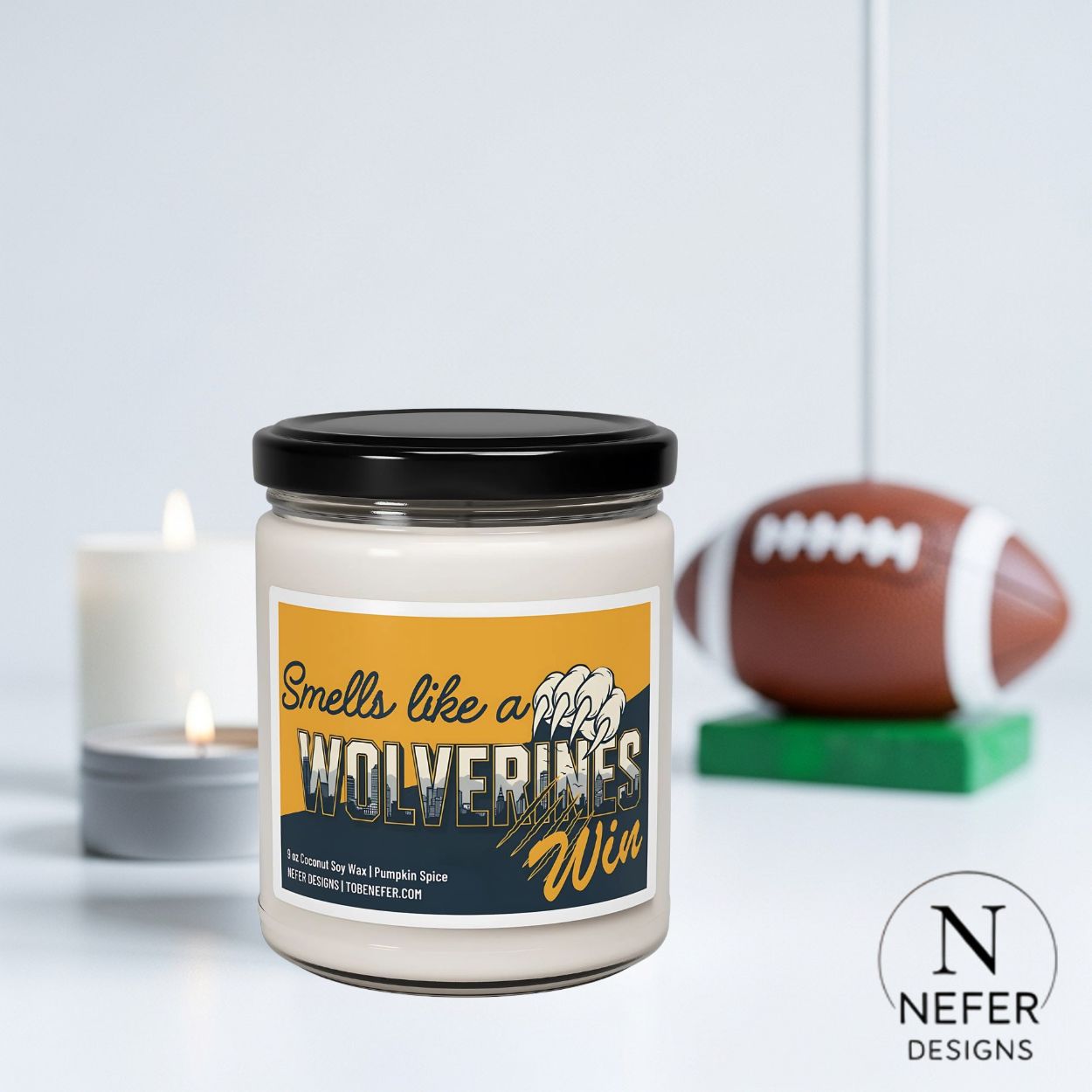 Candle with a label reading 'Smells like a Wolverines Win' next to a football on a light background