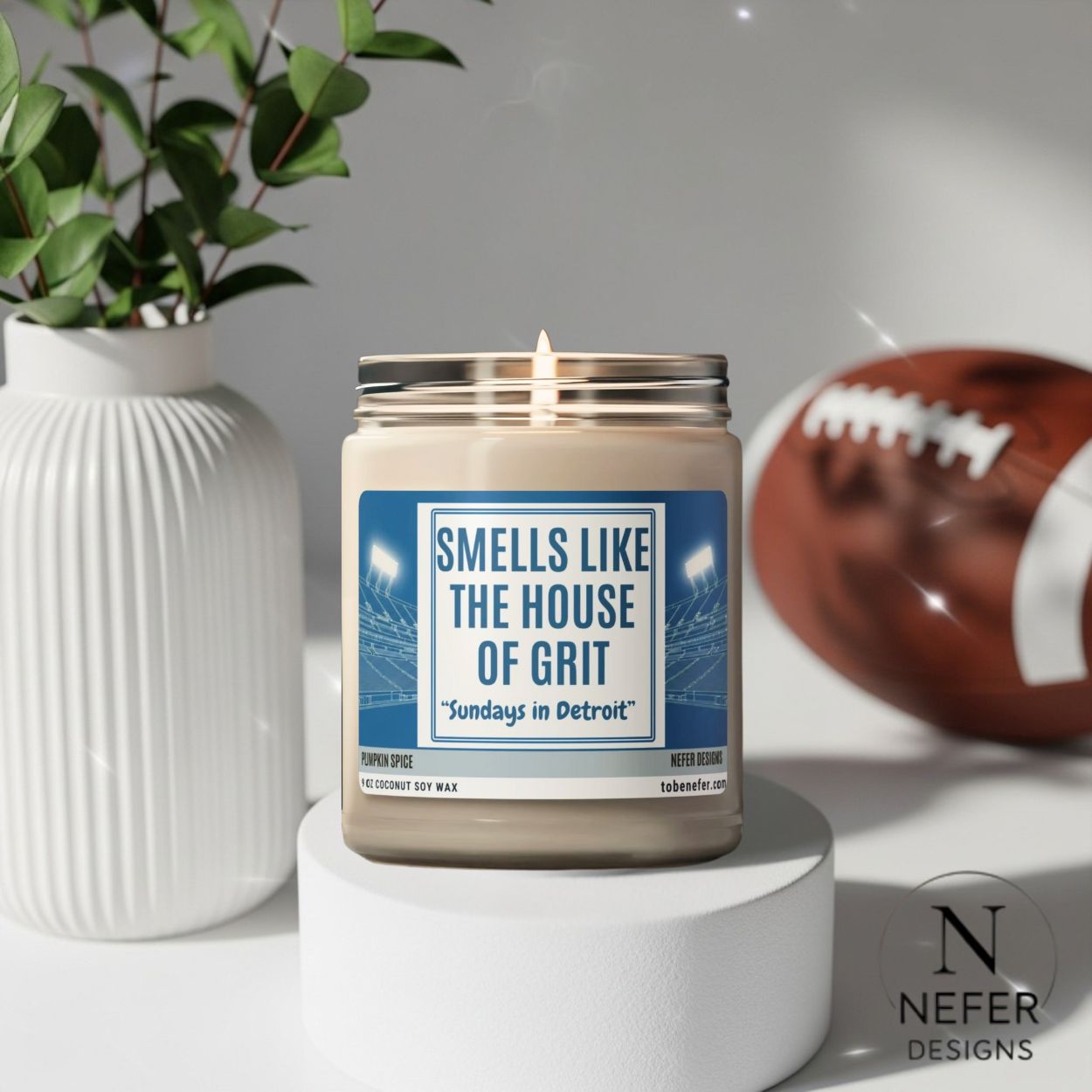 Candle labeled 'Smells Like the House of Grit' by Nefer Designs with a football and plant in the background.