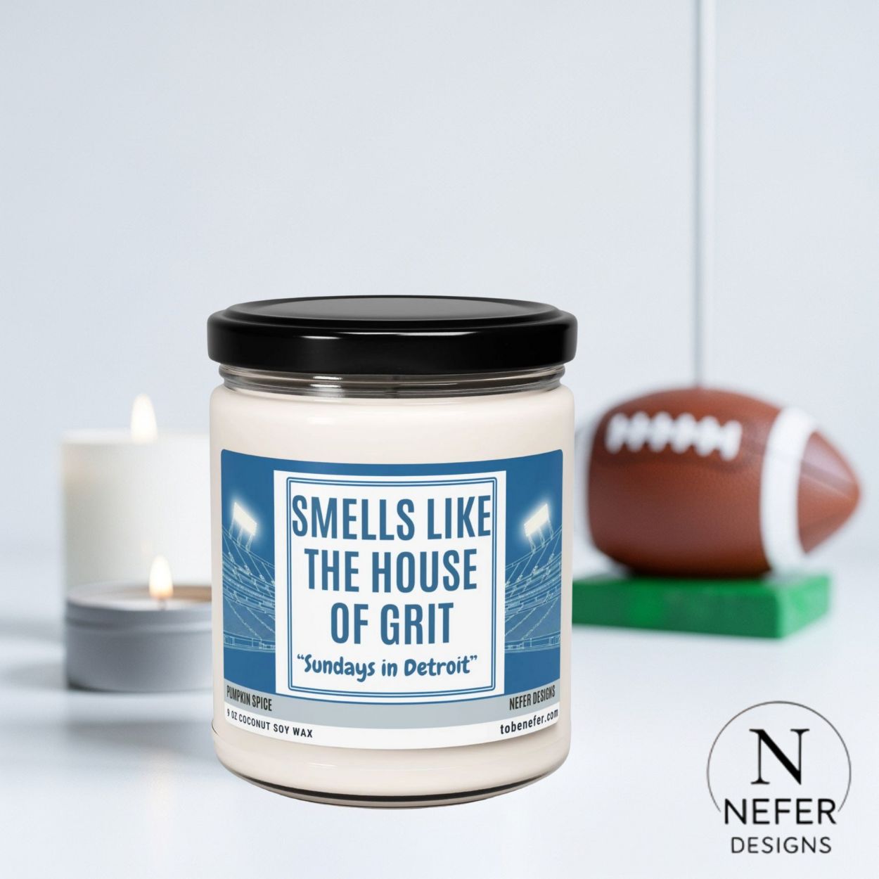 Candle jar with 'Smells Like the House of Grit' label, football, and candle in the background on a light gray background