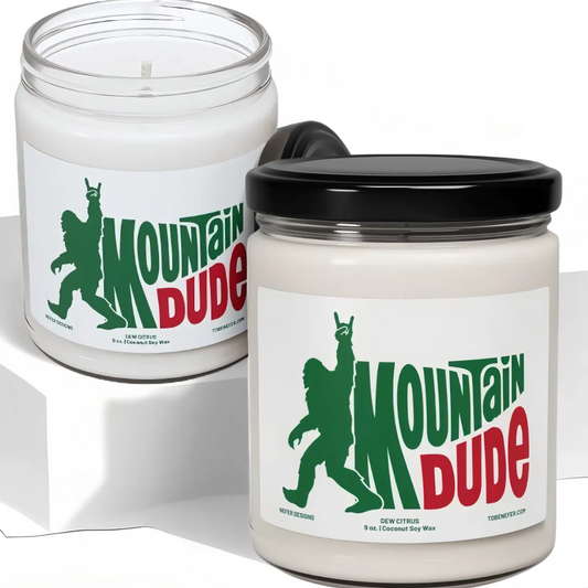 A 9 oz Mountain Dude Soda Pop Soy Candle in a jar, featuring a vibrant bigfoot design with the wording of mountain dude. The candle is hand-poured with a coconut and soy wax blend, offering a refreshing lemon-lime soda scent. Perfect for soda lovers and nostalgia enthusiasts.