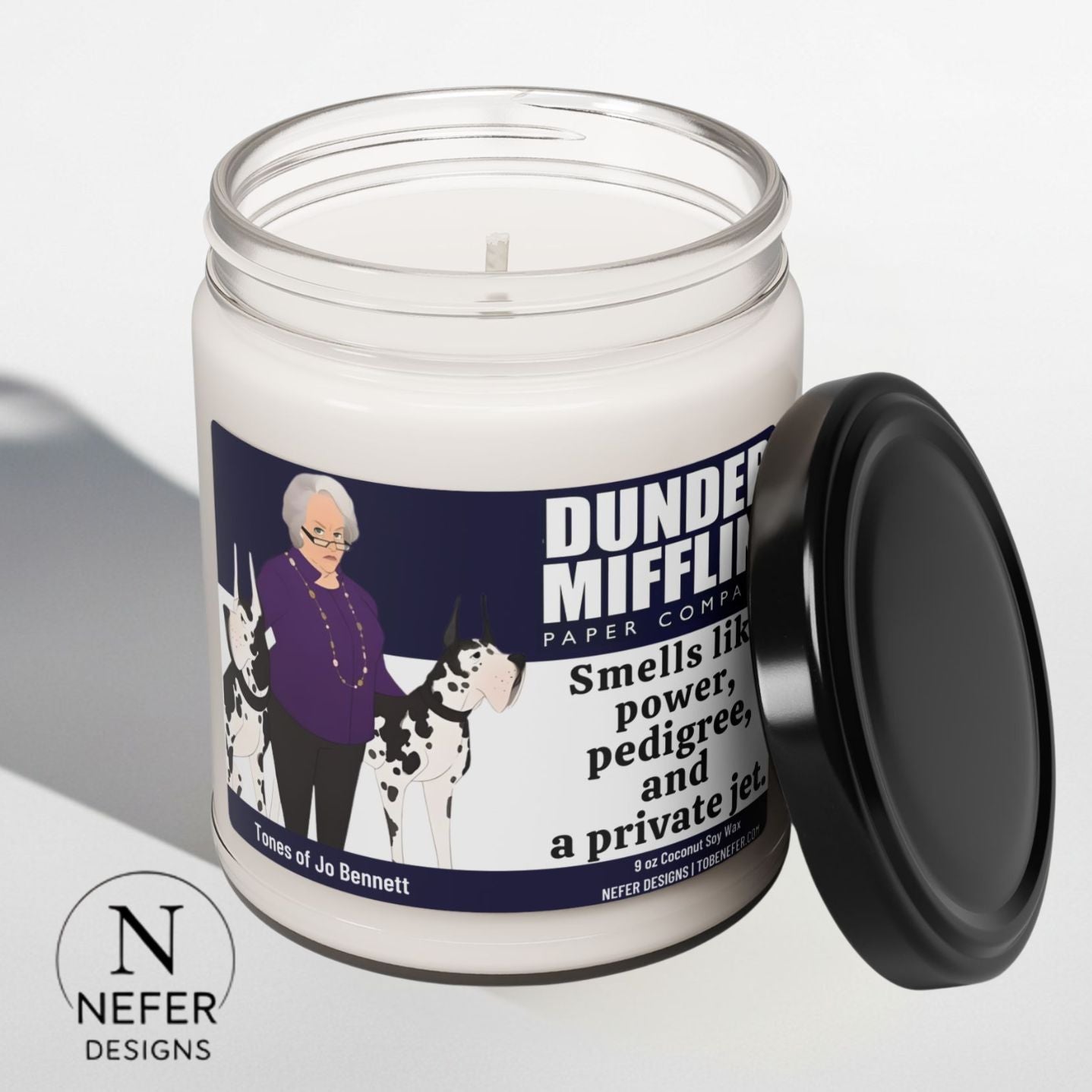 Candle with a label featuring an illustration of a The Office sitcom shoow characterJo Bennett  with dogs and  funny text, on a light gray background.