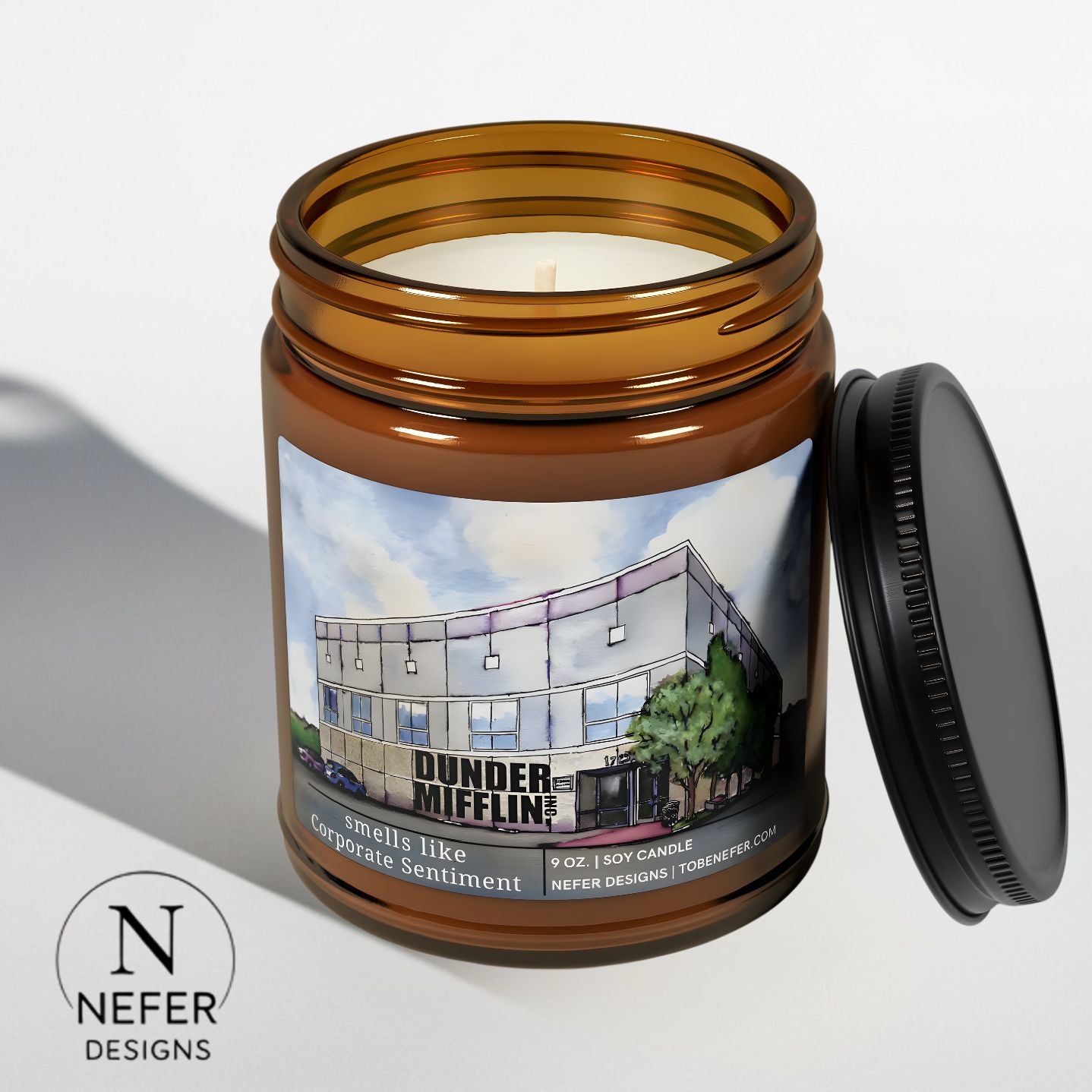 Candle in an amber jar with a labeled design  featuring the office show building of dunder mifflin inc. on a light gray background