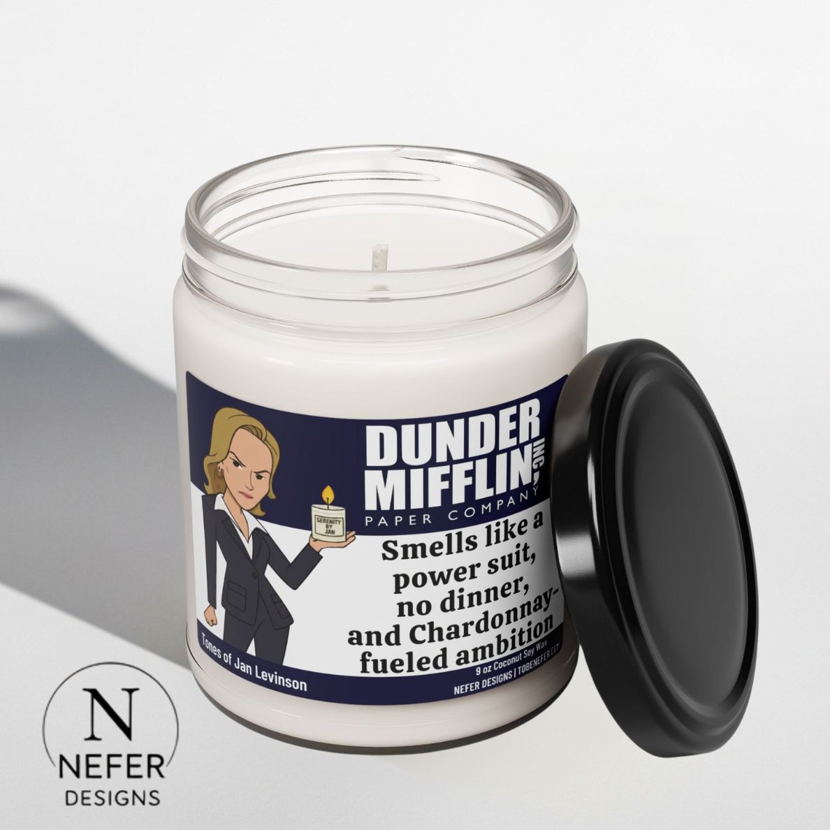 Candle with a 'Dunder Mifflin' label on a white background. The label featuring the cartoon image of Jan holding her candle  with a funny text on the label. Candle located on a white background. 