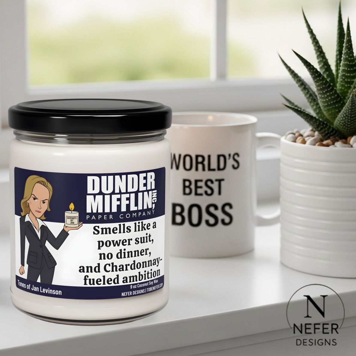 Candle with a funny text related to the office character Jan  character from 'The Office' and a mug with 'World's Best Boss' text, placed on a surface with a plant in the background.